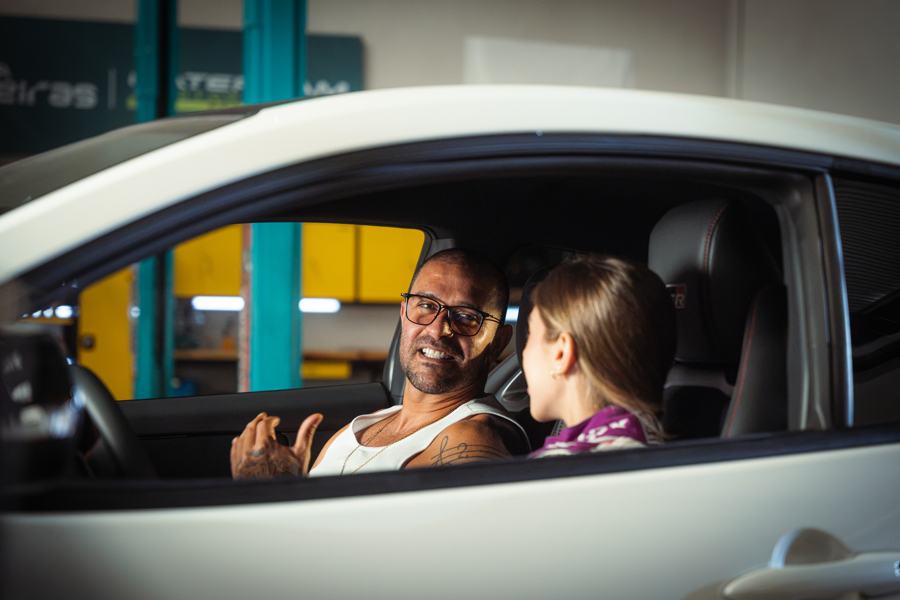 Diogo Nogueira laughing in the driver's seat next to Valentina