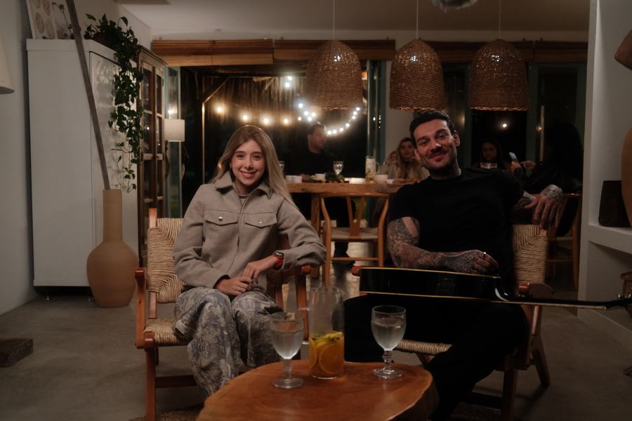 Valentina and Lucas Lucco in a warmly lit lounge, a guitar on his lap